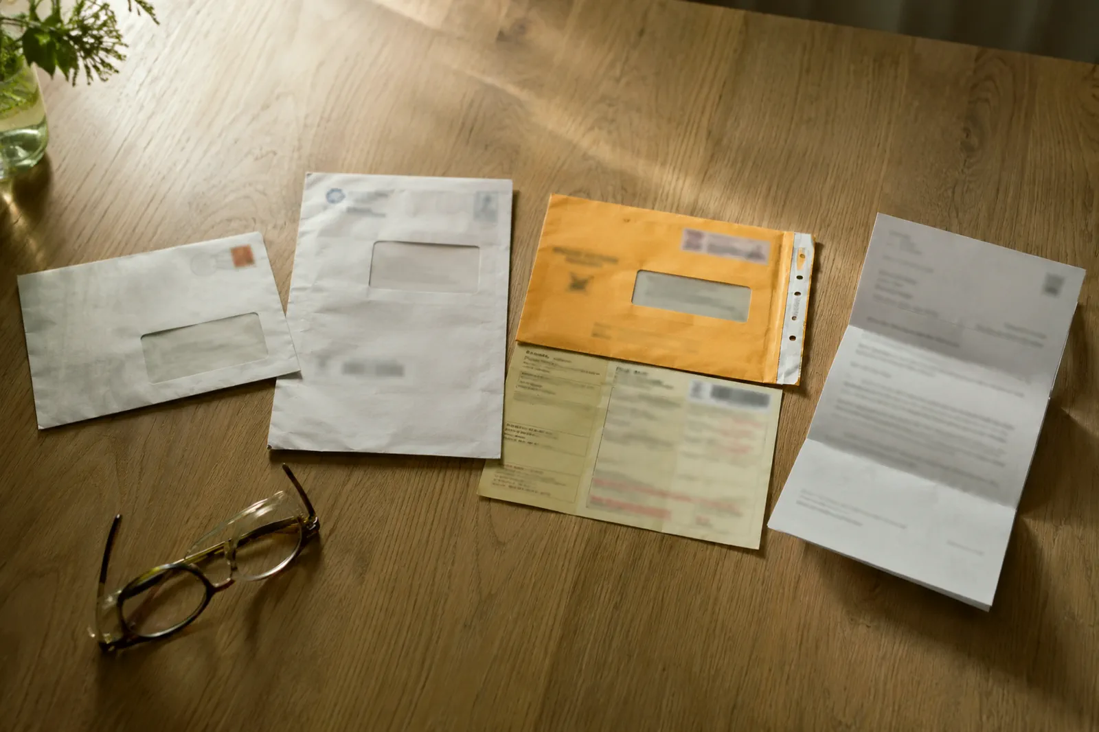 Quatre courriers de la justice sur une table Quatre courriers administratifs étalés sur une table en bois clair : enveloppes à fenêtre, un pli recommandé, un avis jauni et une lettre dépliée, textes illisibles, une paire de lunettes posée à côté.