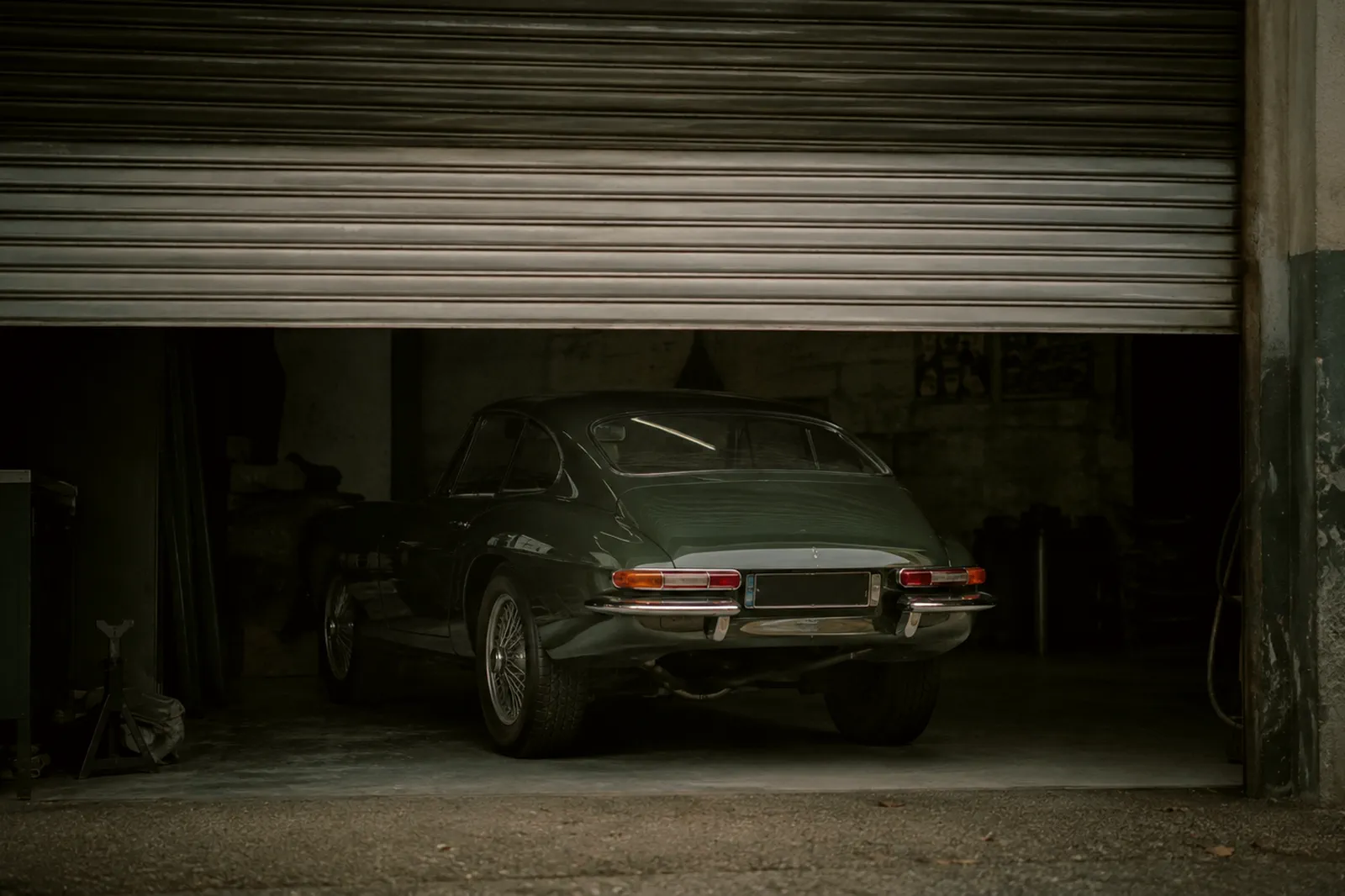 Voiture enfermée derrière un rideau métallique Une voiture ancienne immobilisée dans un garage dont le rideau métallique est à demi baissé.